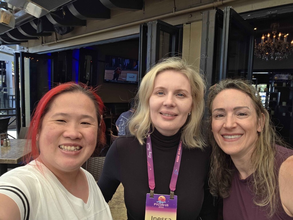 Maintainer Summit co-organizers Leah Wasser, Inessa Pawson, and Mariatta Wijaya smile together for a selfie on an outdoor patio at PyCon US in Long Beach, wearing conference lanyards.